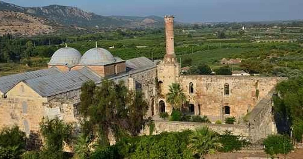 The İsa Bey Mosque in Selçuk seen from the hill above, its twin domes and broken minaret against the orchards