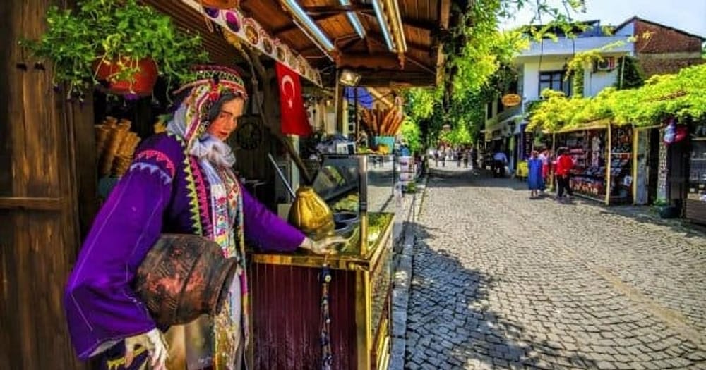 A dondurma seller in traditional embroidered costume at his brass cart on a Şirince lane